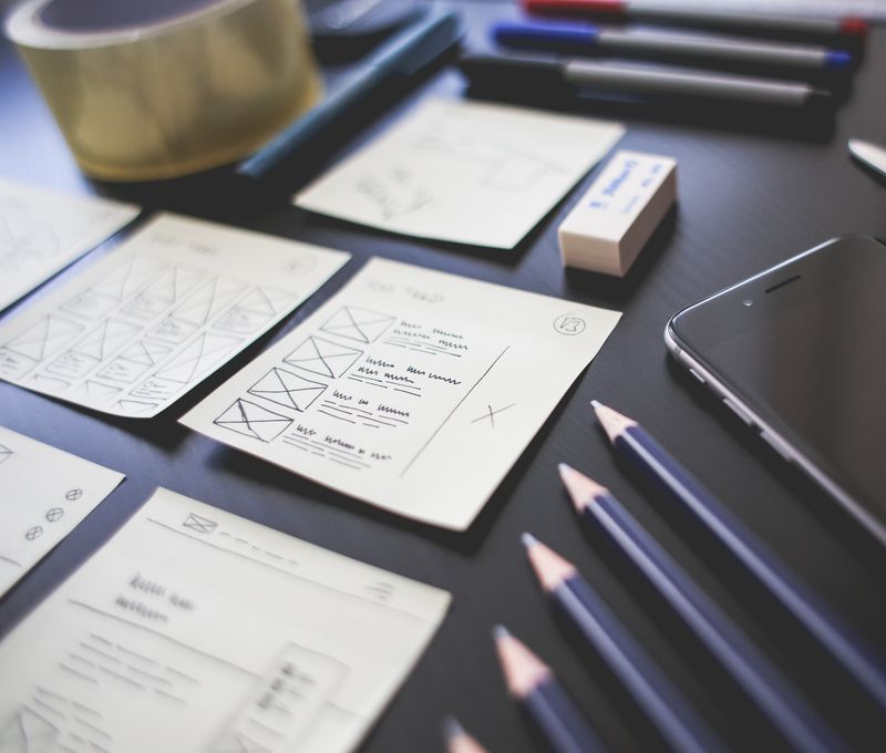 A creative workspace featuring UI design plans, pencils, a smartphone, and other office tools.