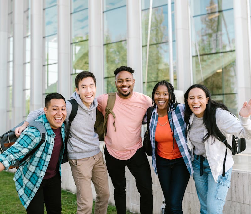 A happy group of diverse college students posing cheerfully outside a modern building.