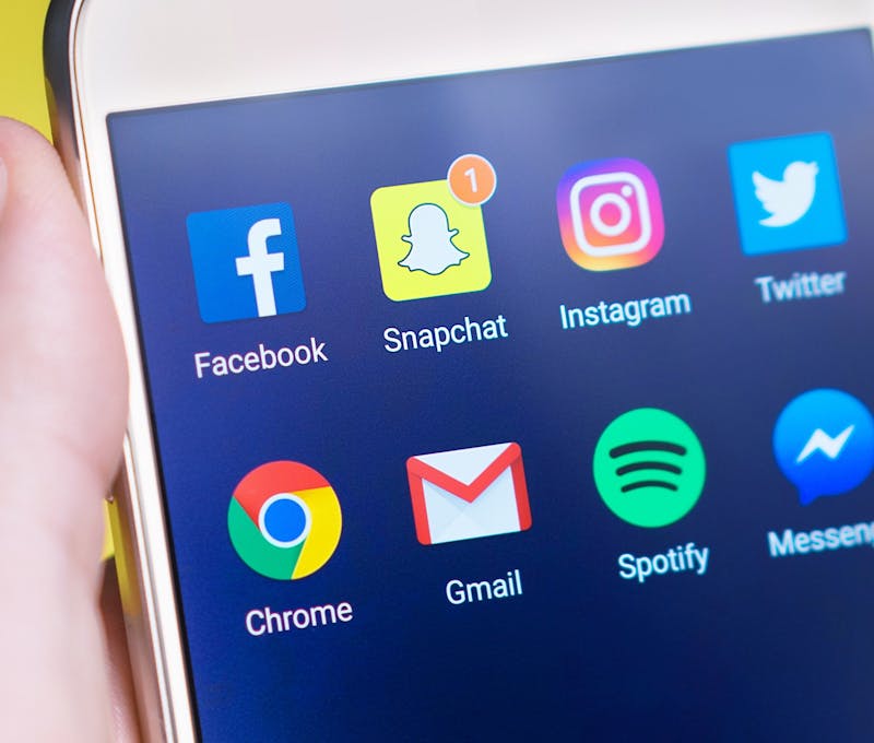 A person's hand holding a smartphone displaying social media and communication apps.