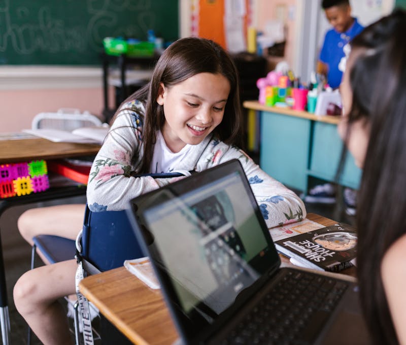 Children engaged in learning with a laptop in a vibrant classroom.