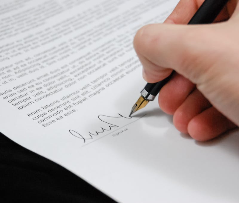 Close-up of a hand signing a legal document with a fountain pen, symbolizing signature and agreement.