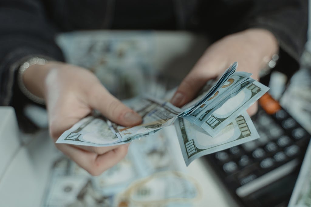 Close-up of hands counting hundred dollar bills with a calculator in the background.