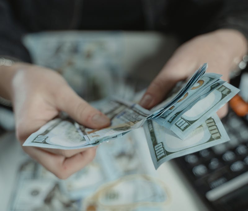 Close-up of hands counting hundred dollar bills with a calculator in the background.