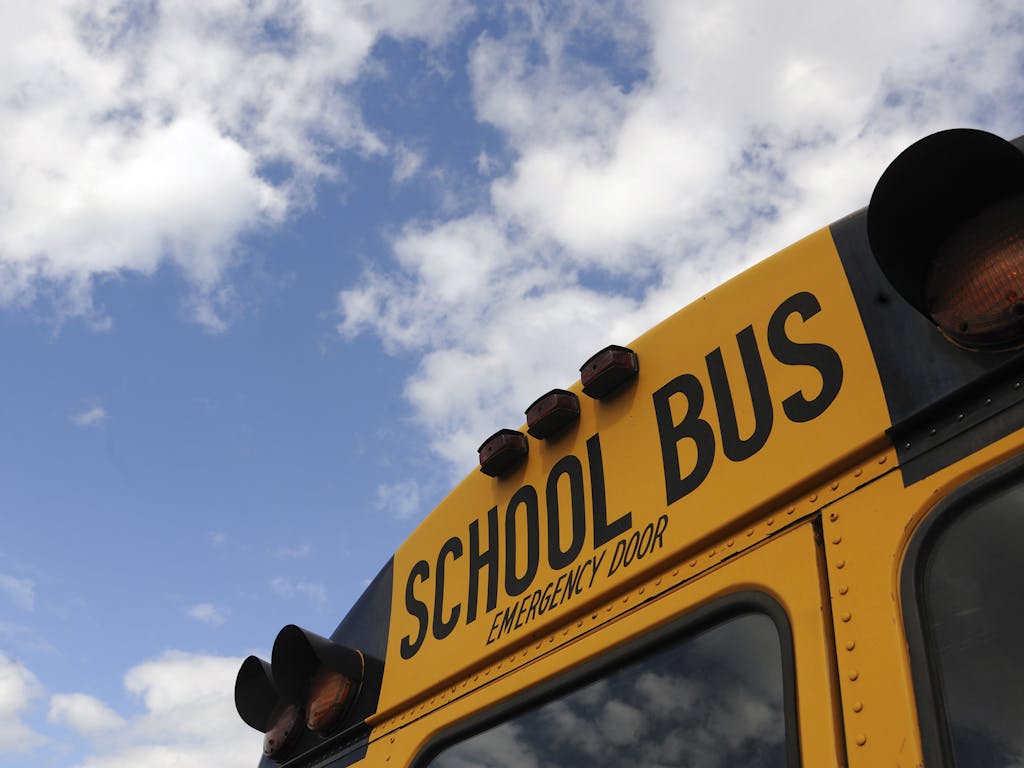 Close-up shot of a yellow school bus with a blue sky background, showcasing cloud formations.