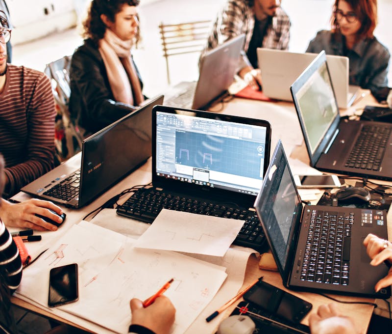 Group of diverse adults collaborating with laptops and papers in a modern office environment.