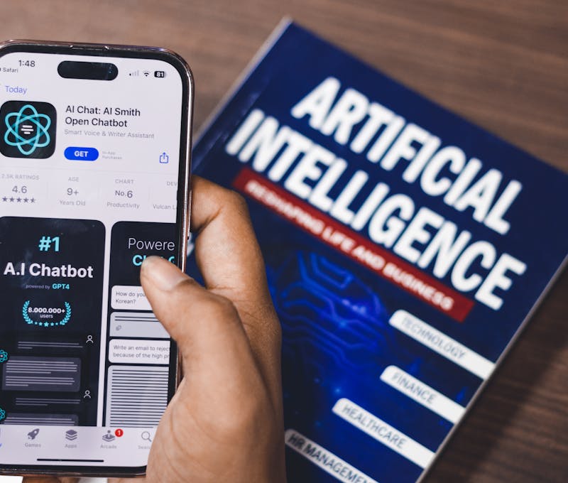 Smartphone displaying AI app with book on AI technology in background.