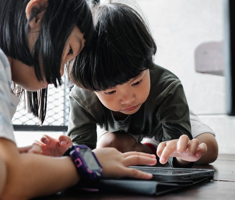Two children focused on using a tablet indoors, engaging with technology for learning and play.