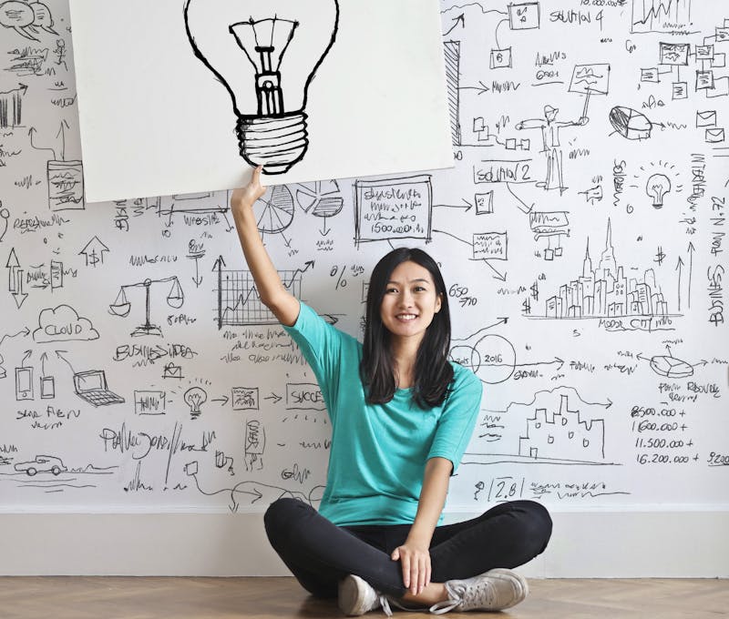 Young woman holds a light bulb drawing against a creative brainstorming wall.